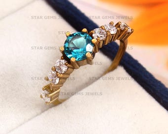 May include: A gold ring with a blue gemstone and white stones. The ring is in a blue velvet box with the words "STAR GEMS JEWELS" printed on the box.
