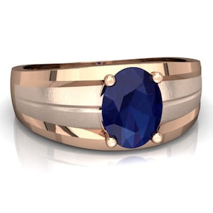 Könnte beinhalten: Ein Ring aus Roségold mit einem blauen ovalen Saphir-Edelstein. Die Band hat eine gebürstete Oberfläche und ein gerilltes Design.