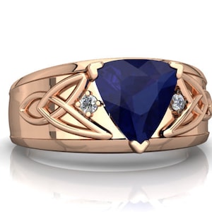Könnte beinhalten: Ein Ring aus Roségold mit einem großen, dunkelblauen, dreieckigen Edelstein, der von zwei kleineren, runden, weißen Edelsteinen umgeben ist. Der Ring hat ein keltisches Knotendesign.