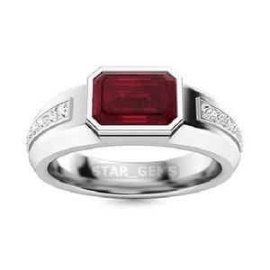 May include: A silver ring featuring a large, rectangular, red ruby gemstone set in a bezel setting. The band is adorned with small, clear diamonds set in a pave setting.