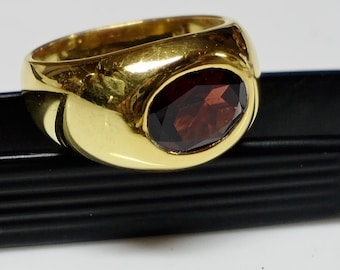 May include: A gold ring with a large, oval-shaped, dark red gemstone set in the center.