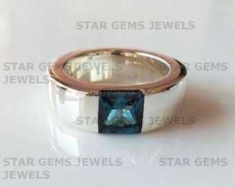 May include: A silver ring with a square blue gemstone set in the center. The ring is wide and has a smooth, polished finish.