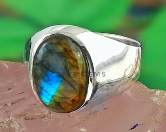 May include: A silver ring with a large oval-shaped labradorite gemstone. The gemstone has a blue, green, and brown iridescent sheen.