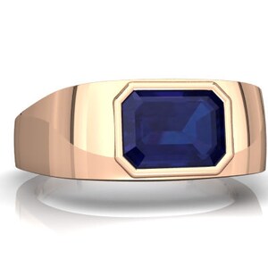 Könnte beinhalten: Ein goldener Ring mit einem großen, rechteckigen, dunkelblauen Edelstein, der in einer Zargenfassung sitzt.