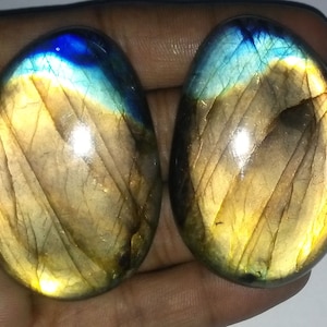 May include: Two oval-shaped labradorite gemstones with a golden and blue iridescent sheen.