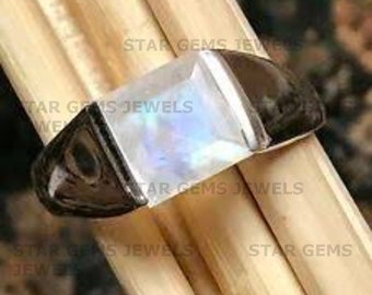 May include: A silver ring with a large, square-shaped moonstone. The stone has a rainbow sheen and is set in a black metal band.