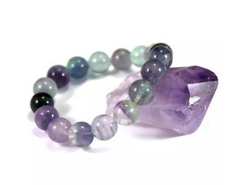 May include: A bracelet made of round, multi-colored fluorite beads. The beads are shades of purple, green, and blue. The bracelet is resting on a large, purple amethyst crystal.