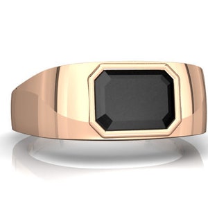 May include: A gold ring with a black gemstone set in a square bezel. The ring has a wide band.