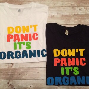 Może przedstawiać: Dwie koszulki z nadrukiem "Don't Panic It's Organic". Koszulki są białe i czarne z nadrukiem w kolorze ż&oacute;łtym, pomarańczowym, zielonym i niebieskim.