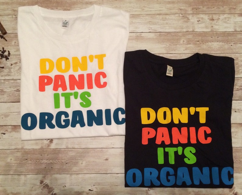 Może przedstawiać: Dwie koszulki z nadrukiem "Don't Panic It's Organic". Koszulki są białe i czarne z nadrukiem w kolorze ż&oacute;łtym, pomarańczowym, zielonym i niebieskim.