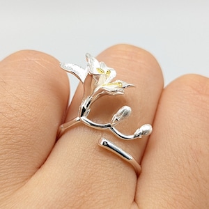 Puede incluir: Un anillo de plata con un delicado diseño de flor. La flor está hecha de metal blanco con detalles amarillos. El anillo es ajustable y se puede llevar en cualquier dedo.