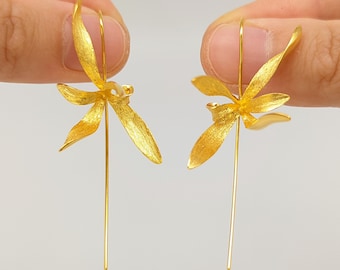 May include: A pair of gold orchid flower dangle earrings. The earrings feature a delicate, detailed orchid flower design with a long, thin gold post.