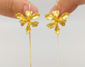 May include: A pair of gold dangle earrings featuring a delicate flower design. The earrings are made of metal and have a long, thin drop.