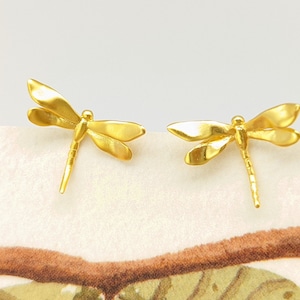 May include: A pair of gold dragonfly earrings. The earrings are made of metal and feature a detailed dragonfly design.