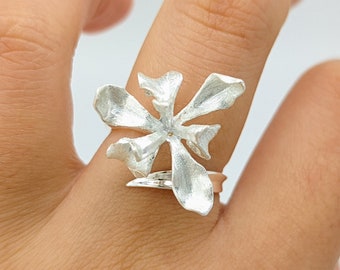 May include: A silver ring with a flower design. The ring is worn on a finger.