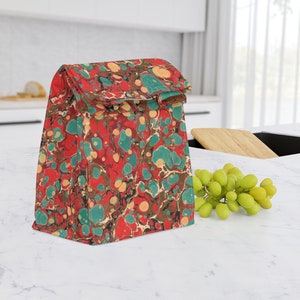 Pode incluir: Uma bolsa de almoço de mármore vermelho, verde e creme com uma parte superior dobrável.