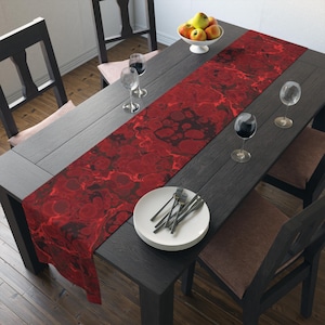 Puede incluir: Un camino de mesa rojo y negro con estampado de mármol sobre una mesa de madera oscura con platos blancos y copas de vino.