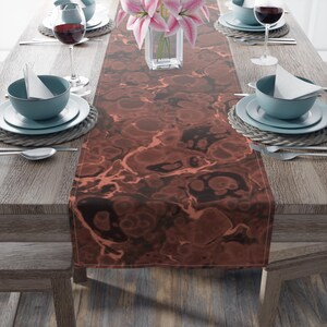 Op de afbeelding: Een bruine en zwarte marmeren tafelrunner met een roze bloemenarrangement in een glazen vaas erop. De runner ligt op een houten tafel met twee couverts aan elke kant.