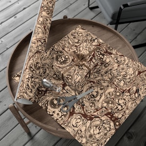 May include: A brown and beige marbled wrapping paper with a gift box wrapped in the same paper. The gift box is tied with a brown ribbon and a bow. There are scissors on the table.
