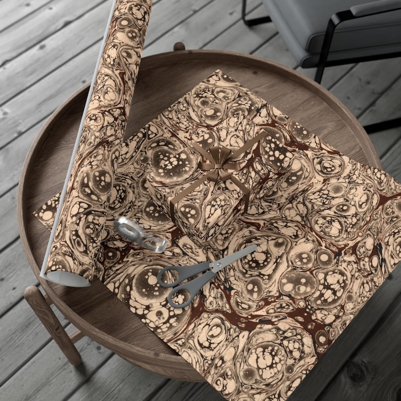 May include: A brown and beige marbled wrapping paper with a gift box wrapped in the same paper. The gift box is tied with a brown ribbon and a bow. There are scissors on the table.
