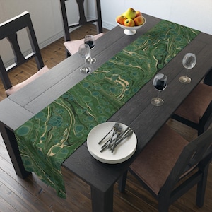 Op de afbeelding: Een groene en witte marmeren tafelrunner met een draaiend ontwerp. De runner ligt op een donkerhouten tafel met twee stoelen en een kom met fruit.