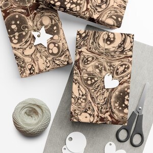 May include: Three gift boxes wrapped in brown paper with a marbled pattern in shades of brown and white. The boxes are tied with twine and decorated with white paper stars and hearts.
