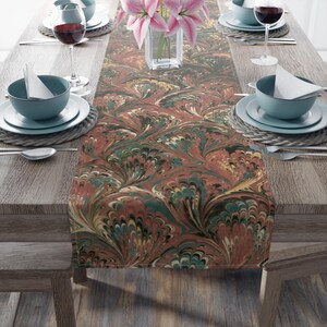 Op de afbeelding: Een bruine, groene en witte marmeren tafelrunner met een draaiend patroon. De runner ligt op een houten tafel met couverts aan beide kanten.