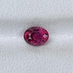 Könnte beinhalten: Ein oval geschliffener Edelstein in einer tiefen, leuchtenden magentaroten Farbe. Der Stein besitzt eine facettierte Oberfläche, die ein komplexes Muster aus hellen und dunklen Reflexionen erzeugt und ein klares, brillantes Aussehen bietet.