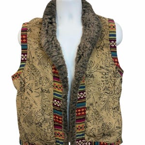 May include: A tan suede vest with a brown faux fur collar and colorful geometric patterned trim. The vest has a printed design of abstract symbols and lines.