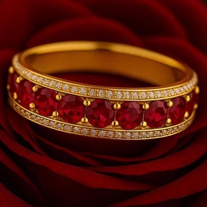 Może przedstawiać: Złoty pierścionek z rzędem żywych, czerwonych kamieni szlachetnych, zaakcentowanych małymi diamentami. Pierścionek osadzony jest na głębokim, czerwonym tle, tworzącym uderzający kontrast. Biżuteria.