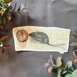 Puede incluir: Una pegatina con una ilustración de mosaico de un ratón con una concha roja y marrón. El ratón es gris y tiene una cola larga. El mosaico está hecho de pequeñas baldosas de colores.