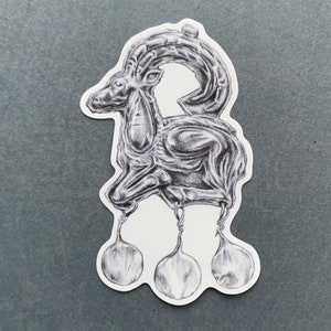 May include: A black and white drawing of a stylized goat with three dangling balls at the bottom. The goat is depicted in a standing position with its head turned to the side.