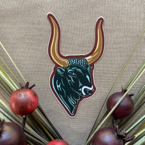 May include: A sticker of a black bull's head with gold horns and a blue and green patterned headpiece.
