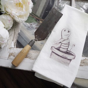 Puede incluir: Una toalla de cocina blanca con una ilustración dibujada a mano de un gusano en una maceta con la palabra "silencio" escrita en la maceta.