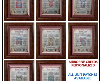 May include: A collection of eight framed United States Army Airborne Creed documents, each featuring aged parchment paper, a maroon mat, and a dark wood frame. Each document displays a unique military unit patch and insignia at the center.