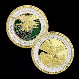 May include: Two gold-colored challenge coins. The first coin features a green and white emblem with the text "UNITED STATES NAVAL SPECIAL WARFARE COMMAND". The second coin features a gold-colored emblem of three figures in a triangular formation with the text "US. NAVY SEALS" and "SEA, AIR, LAND" around the emblem.