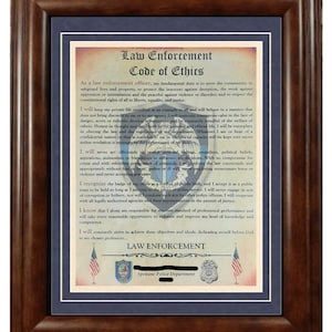 May include: A framed document with a blue background and gold trim. The document is titled "Law Enforcement Code of Ethics" and includes a code of conduct for law enforcement officers. The document also features the Spokane Police Department logo.
