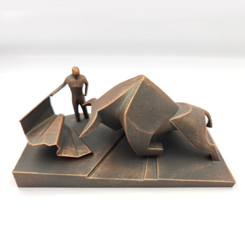 May include: A bronze sculpture of a bullfighter facing a charging bull. The bull is made of geometric shapes and the bullfighter is holding a cape. The sculpture is on a rectangular base.