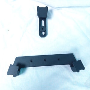 May include: Two black 3D printed plastic pieces for mounting a camera. The larger piece has four holes and two angled ends. The smaller piece has a single hole and a rectangular shape.