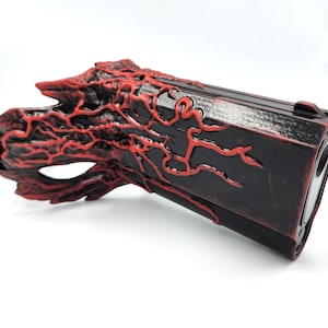 Könnte beinhalten: Eine schwarze und rote Maskenballmaske mit einem detaillierten Design eines Baumes mit roten Adern. Die Maske hat ein schwarzes Gummiband.