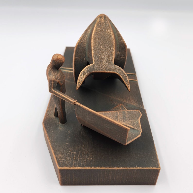 May include: A bronze-colored sculpture of a person pushing a cart with a rocket ship on top. The sculpture is on a rectangular base.