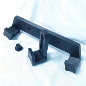 May include: A black 3D printed wall mount with two hooks. The mount has a rectangular base with two side arms that extend out and up. The hooks are located at the end of each arm.