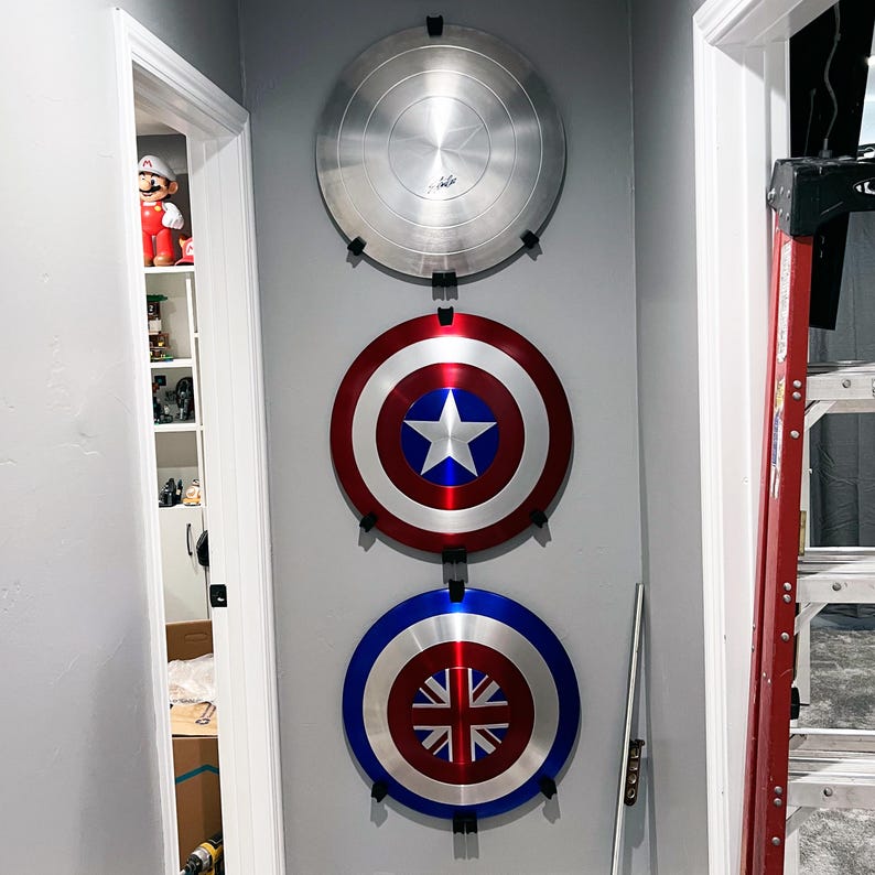 May include: Three round metal shields mounted on a wall. The top shield is silver, the middle shield is red, white, and blue, and the bottom shield is red, white, and blue with a Union Jack design.