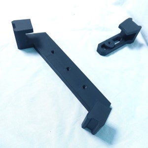 May include: Two black plastic 3D printed wall mounts. The larger mount has four holes and a curved shape. The smaller mount has a straight shape and a single hole.