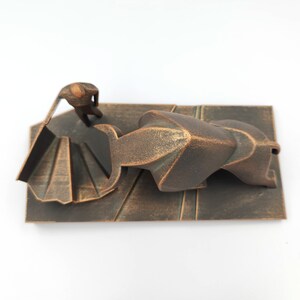 May include: A bronze sculpture of a person standing on a staircase, looking down at a large, abstract bronze form.