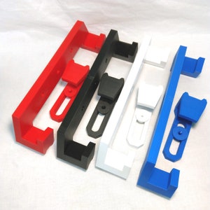 May include: Four wall-mounted storage brackets in red, black, white, and blue. Each bracket has a rectangular shape with a rounded edge and a small, rectangular opening in the center. The brackets are made of plastic and have a smooth, glossy finish.