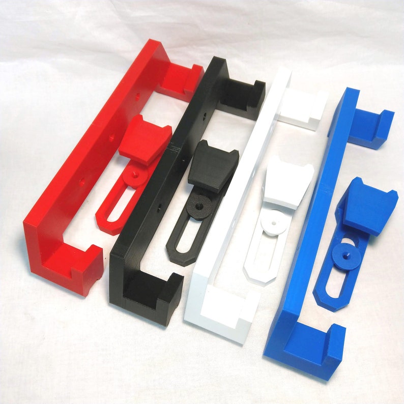 May include: Four wall-mounted storage brackets in red, black, white, and blue. Each bracket has a rectangular shape with a rounded edge and a small, rectangular opening in the center. The brackets are made of plastic and have a smooth, glossy finish.
