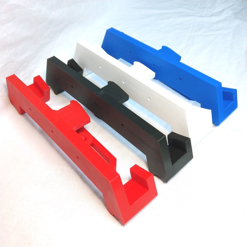 May include: Four 3D printed wall mounts in red, black, white, and blue. The mounts are designed to hold a variety of items, such as pictures, mirrors, or shelves.