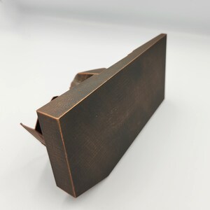 May include: A dark brown metal sculpture of a building with a textured surface. The sculpture is on a white background.