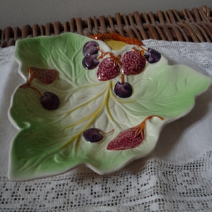 May include: A green ceramic leaf-shaped serving dish with raised details of berries and leaves. The dish is decorated with purple, red, and yellow accents.